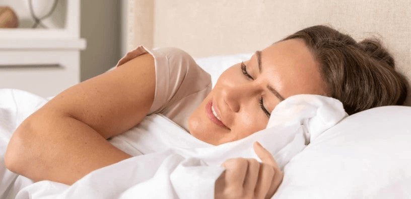 A woman is smiling while sleeping, holding a cosy, white bed sheet.