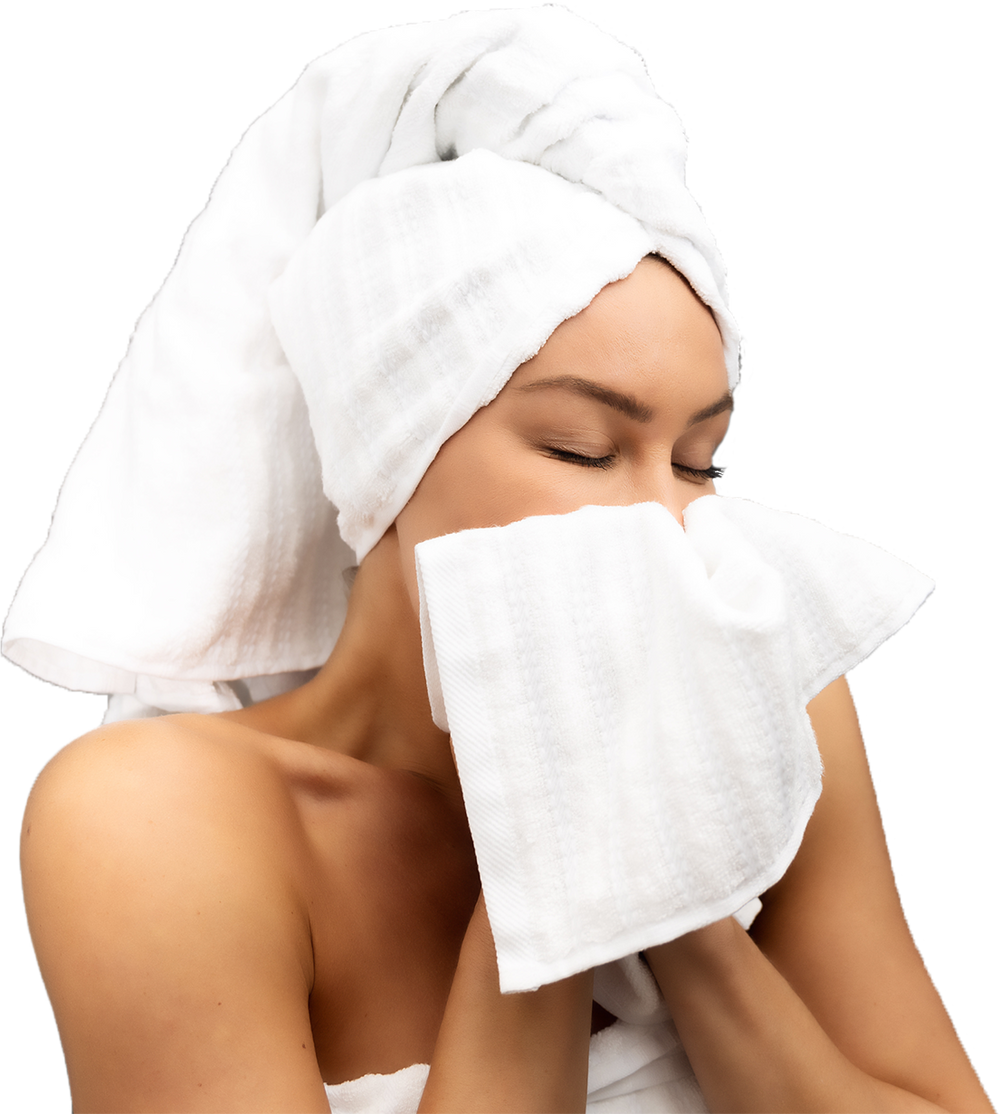 Woman with towel-wrapped hair drying her face with a white towel, eyes closed in a peaceful, fresh-out-of-shower moment.