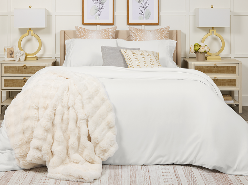 Neatly made bed with white bedding and decorative pillows in a bedroom setting.