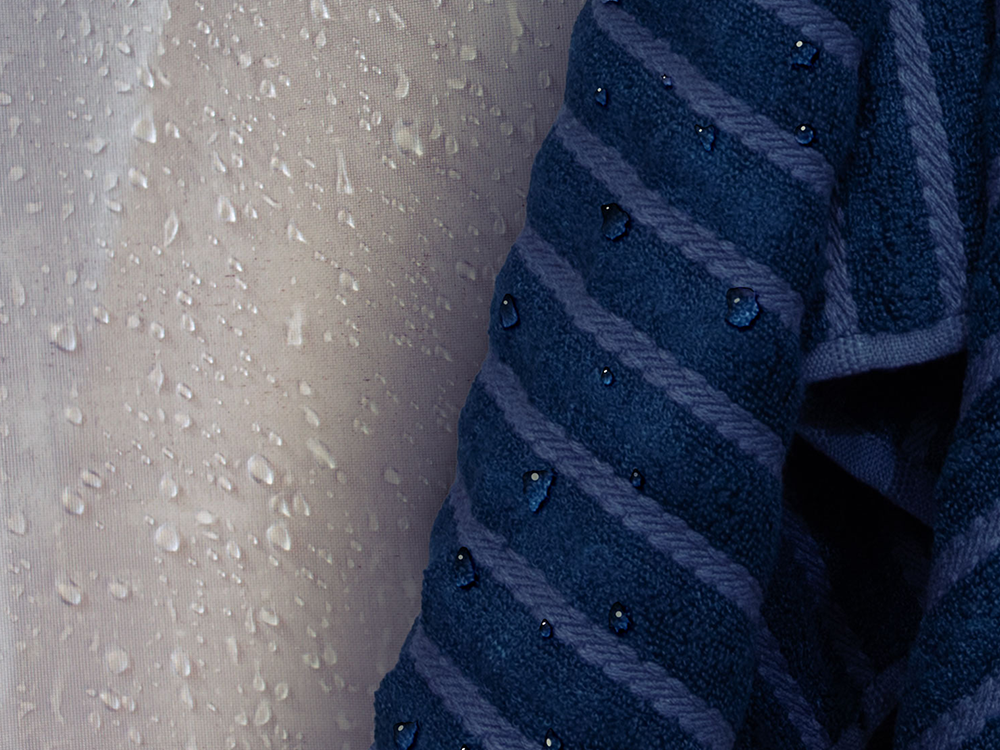 Close-up of a navy striped towel with water droplets, hanging beside a wet shower curtain.